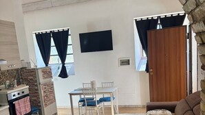 Une pièce meublée comprenant un canapé, une table à manger avec des chaises, un téléviseur et un coin cuisine équipé d’une cuisinière et de placards.