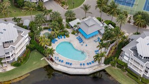 Ein Resort mit einem zentralen Schwimmbad, mehreren Liegebereichen und einem Tennisplatz.