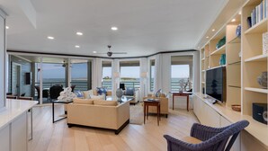 A modern living room with a sofa, chairs, a television, and a bookshelf. - 1617 Lands End Village | Best View on Captiva! (Captiva)