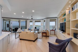 Ein modernes Wohnzimmer mit einer Couch, Sesseln, einem Fernseher und einem Bücherregal.