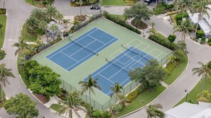 An aerial view of a tennis court surrounded by palm trees and a parking area. - 1617 Lands End Village | Best View on Captiva! (Captiva)