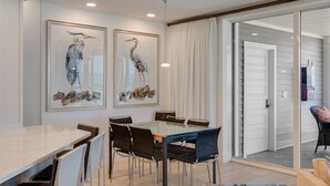 A dining area with a glass-top table, black chairs, and two framed artworks on the wall. - 1617 Lands End Village | Best View on Captiva! (Captiva)