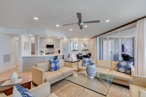 A modern living room with a sofa, coffee table, and a dining area with a kitchen in the background. - 1617 Lands End Village | Best View on Captiva! (Captiva)