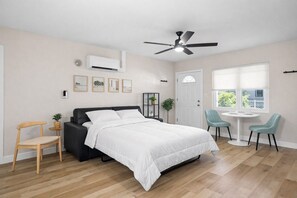 Quarto com cama, ventoinha no teto, janela e uma mesinha com cadeiras.