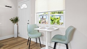 A room with a white door, a window with a view of greenery, two chairs, and a small table. - 221 Madison Ave - Unit B (Cape Canaveral)