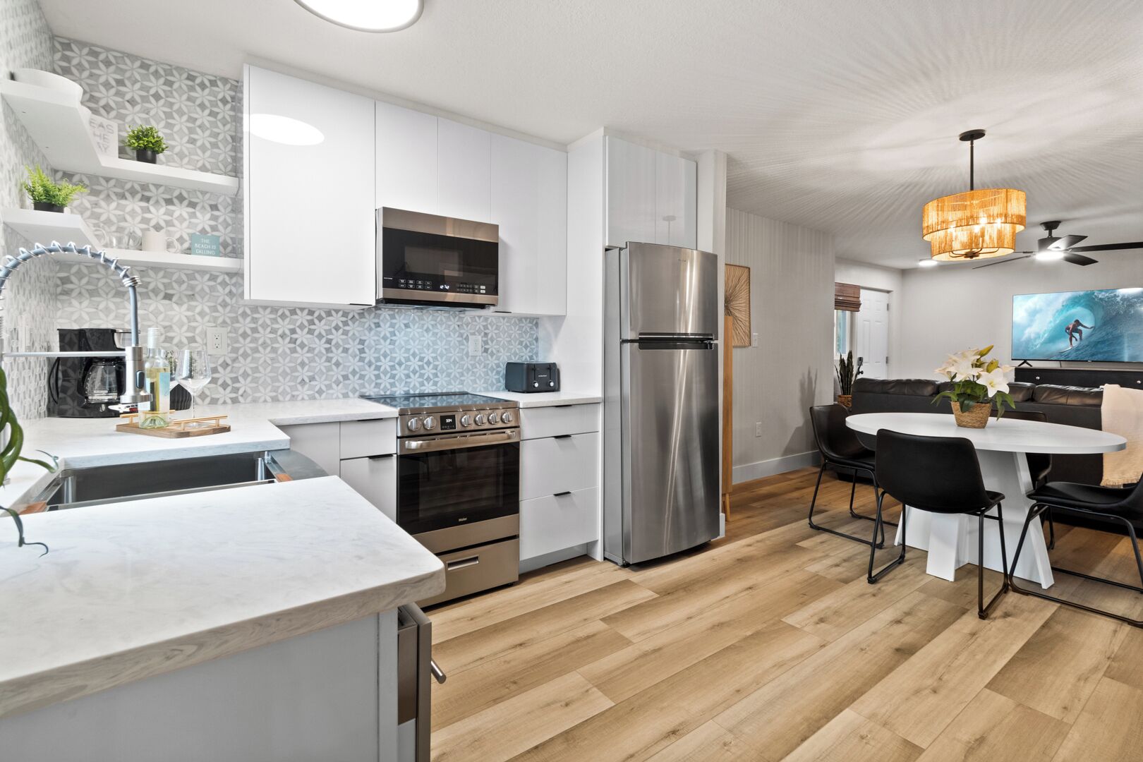 A modern kitchen with stainless steel appliances, a dining area with a round table, and a living room with a flat-screen TV.