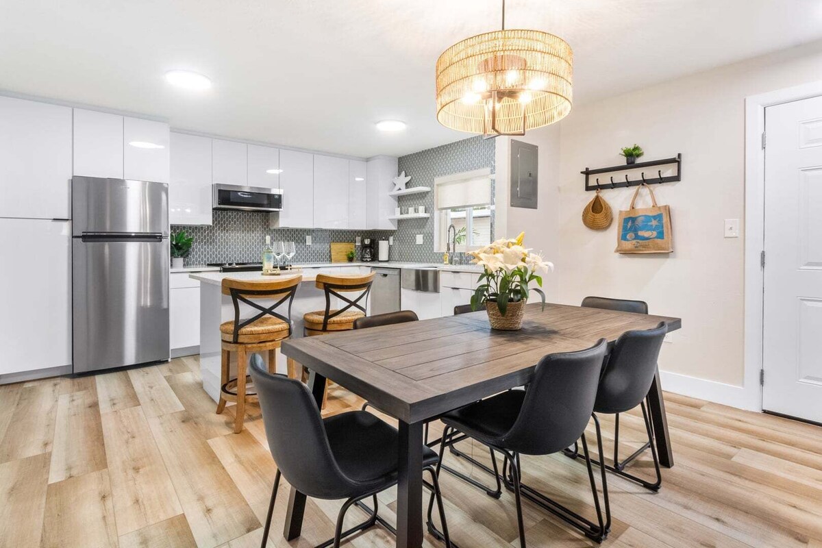 A modern kitchen with white cabinets, a stainless steel refrigerator, and a dining area with a wooden table and black chairs.