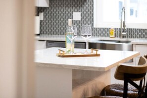 A kitchen with a marble countertop, a bottle of water, and two glasses on a wooden tray. - 221 Madison Ave - Unit B (Cape Canaveral)