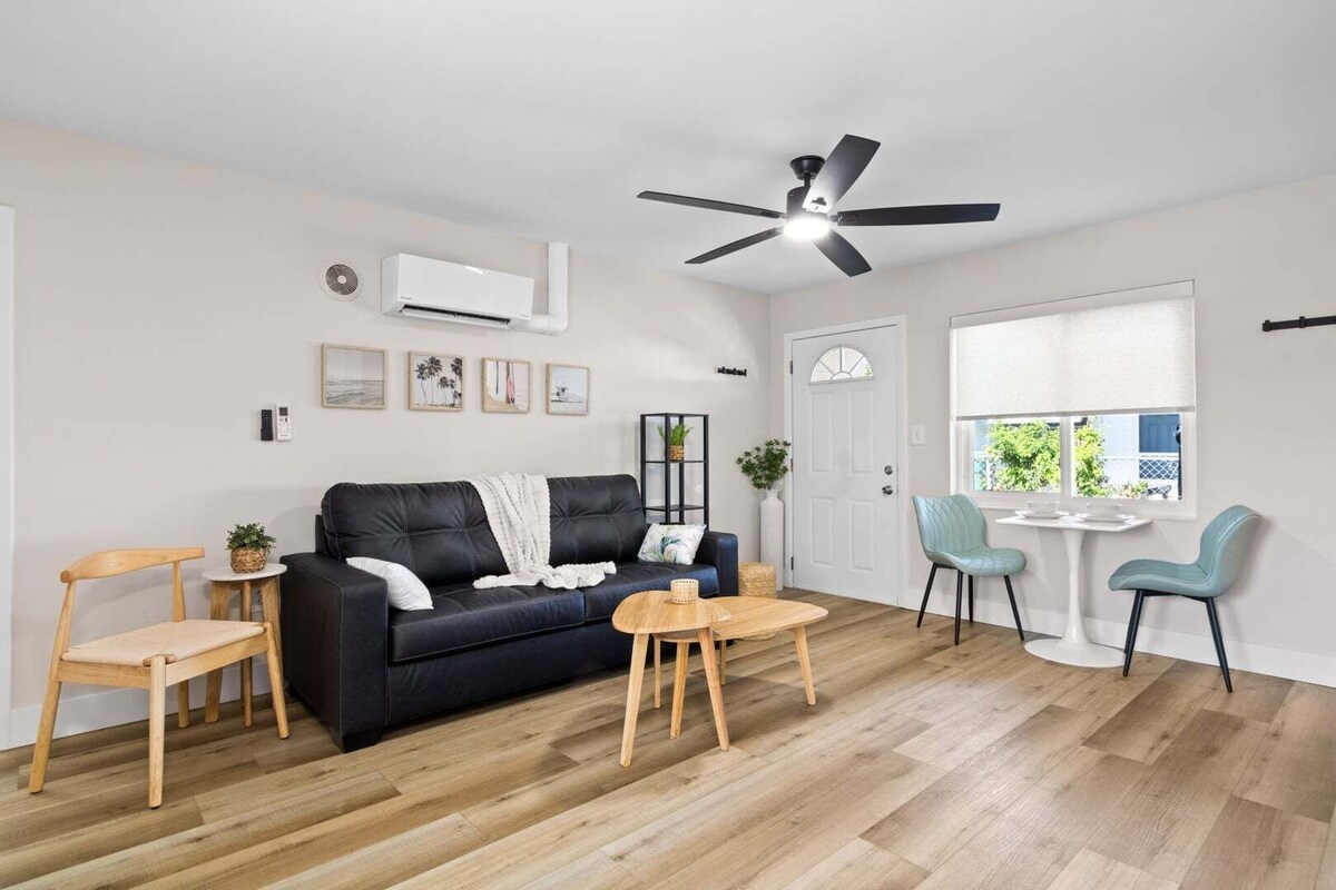 A modern living room with a black leather sofa, wooden coffee table, and two chairs.