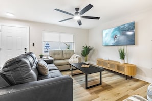 A modern living room with a sofa, armchair, coffee table, and a TV mounted on the wall. - 221 Madison Ave - Unit B (Cape Canaveral)