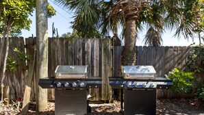 Two outdoor grill stations with wheels, set against a wooden fence and palm tree, in a backyard. - 221 Madison Ave - Unit B (Cape Canaveral)