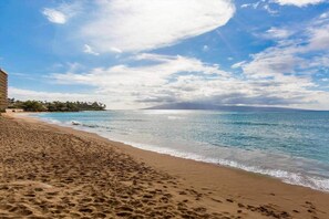 Ein Strand mit einem Gebäude links, blauem Himmel und ruhiger See.