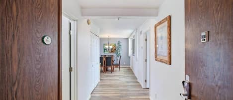 A hallway with wooden doors, a dining area with a table and chairs, and a plant.