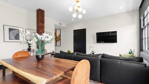 A modern living room with a wooden dining table, a black leather sofa, a mounted TV, and a wooden accent wall. - The Perfect Layout for a Memorable Stay! All Kings (New Orleans)