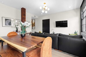 A modern living room with a wooden dining table, a black leather sofa, a mounted TV, and a wooden accent wall. - The Perfect Layout for a Memorable Stay! All Kings (New Orleans)