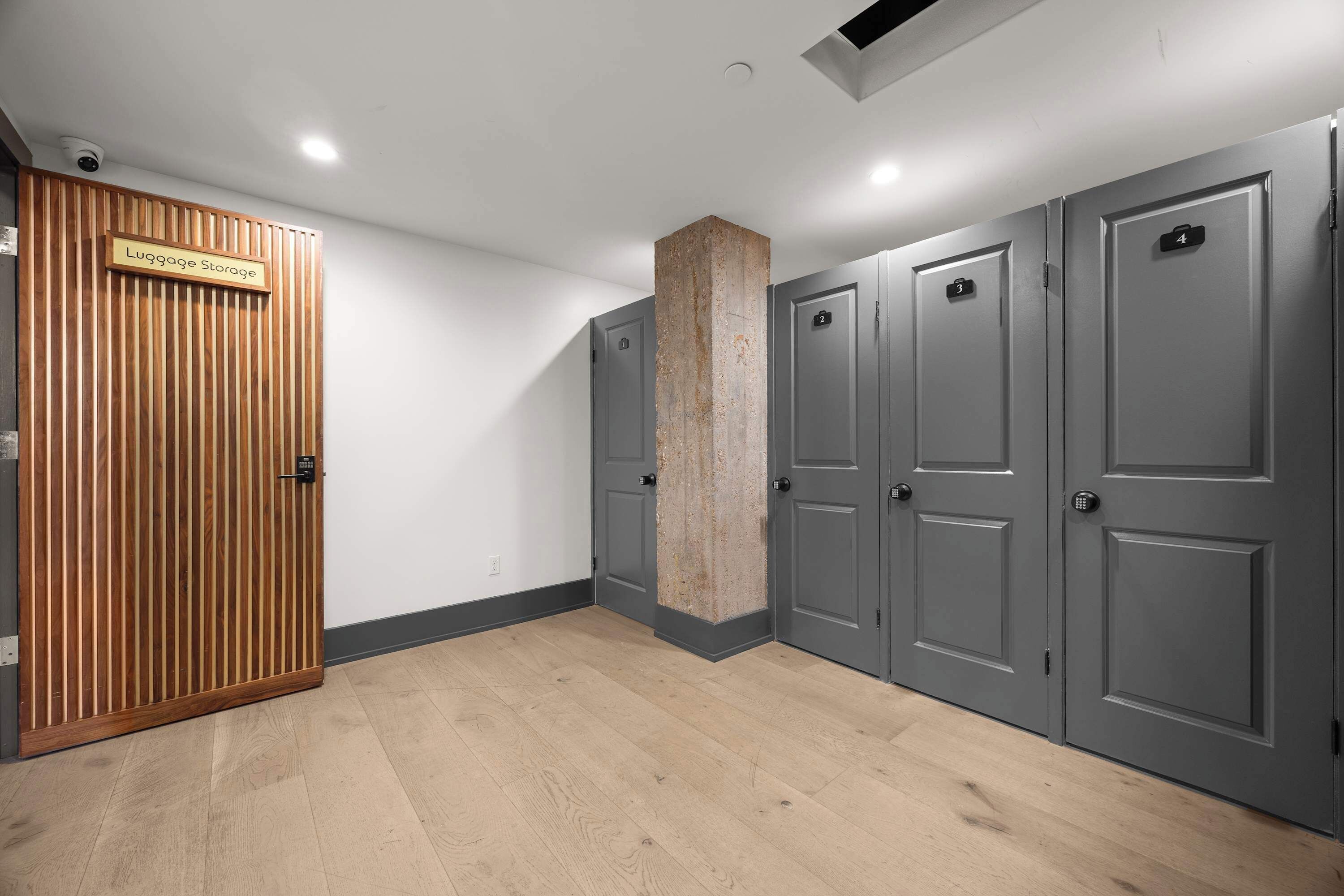 Une chambre d’hôtel dotée d’un espace de rangement pour les bagages, de portes grises et d’un mur recouvert de panneaux en bois.
