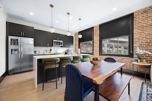 A modern kitchen with a central island, dark cabinets, stainless steel appliances, and a large window with a view of the city. - 3BR Suite W/ Queen Sofa Hotel (New Orleans)
