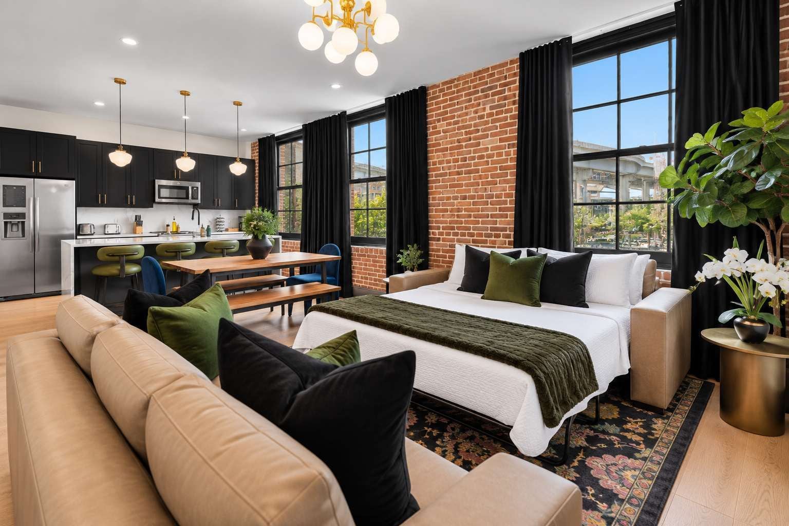 A modern hotel room with a large bed, a sofa, a dining area, and a kitchen.