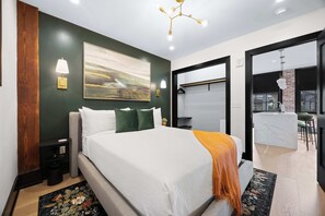A modern bedroom with a large bed, a painting, a desk, and a view of the outside. - Luxury 3BR Suite W/ Queen Sofa (New Orleans)