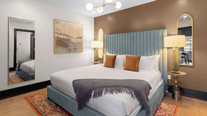 Een hotelkamer met een groot bed, twee bedlampen, een spiegel en een schilderij aan de muur.