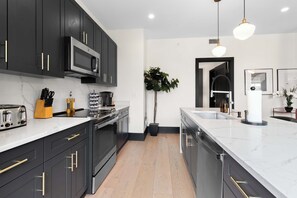 A modern kitchen with dark cabinetry, a stainless steel range, and a large island with a sink. - 2 KING BEDS + SLEEPER SOFA + ROOFTOP + GYM + GAMES (New Orleans)