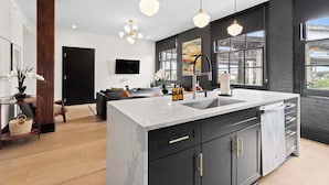 Een moderne keuken met een groot eiland, zwarte kasten en hangende lampen.