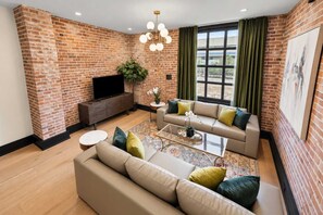 A living room with a brick wall, a sofa set, a coffee table, and a television. - All Suites Hotel | 24/7 Staff | Safe | Secure (New Orleans)