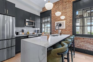 A modern kitchen with dark cabinetry, stainless steel appliances, and a marble island. - Boutique 1BR Suite | Rooftop | Convention Ctr (New Orleans)