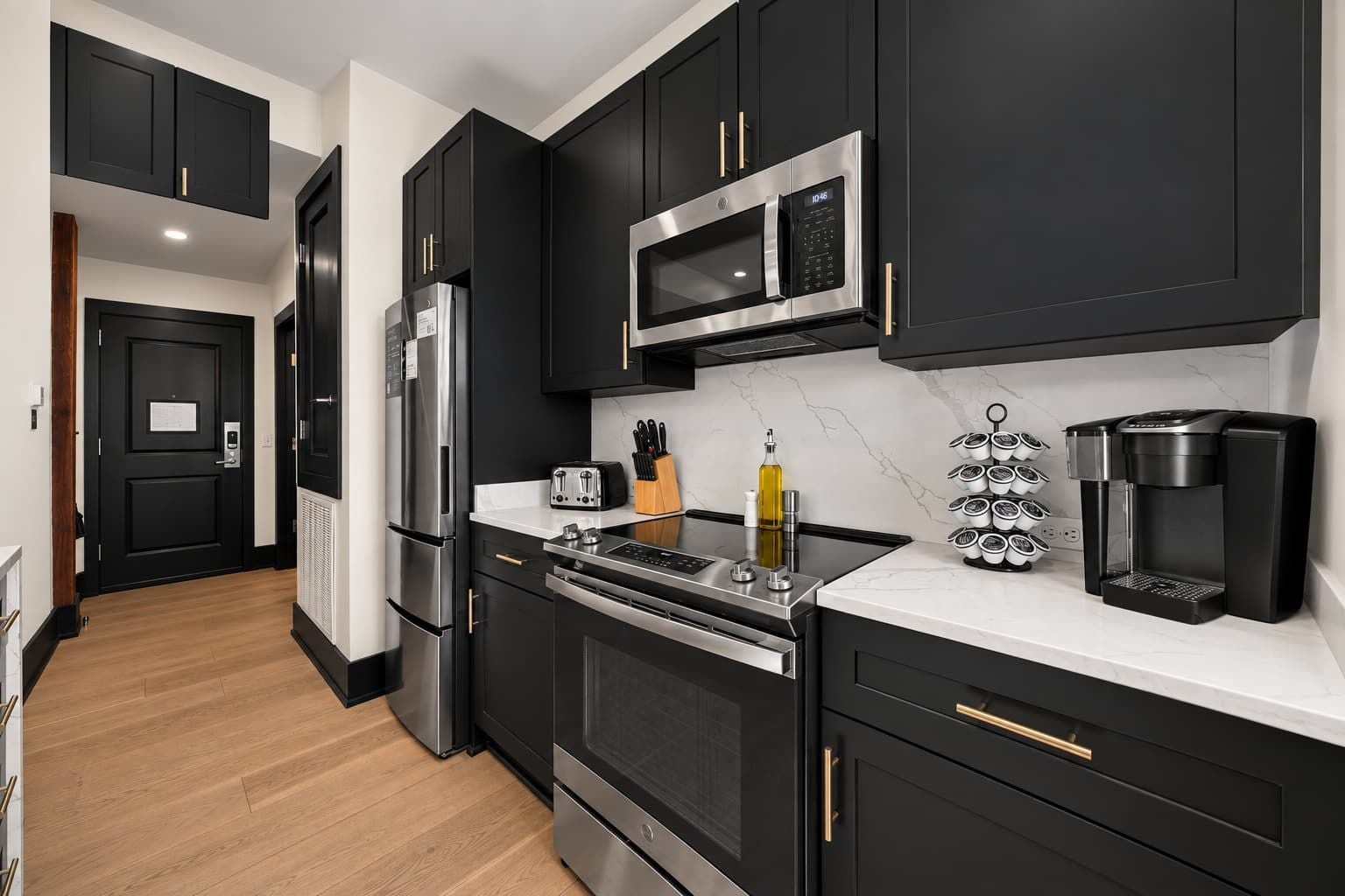 A modern kitchen with black cabinetry, stainless steel appliances, and a marble countertop.
