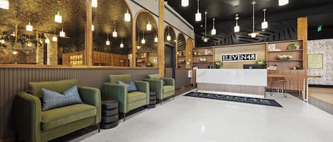 A hotel lobby with green sofas, a reception desk, and a sign reading 'ELEVEN48'.