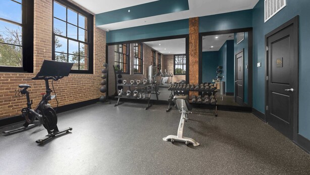 Ein Fitnessstudio mit Trainingsgeräten, großen Fenstern und einer Ziegelwand.