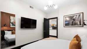 Ein Hotelzimmer mit einem Bett, einem Flachbildfernseher, einem Gemälde und einer Tür zu einem anderen Raum.