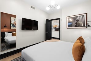 Ein Hotelzimmer mit einem Bett, einem Flachbildfernseher, einem Gemälde und einer Tür zu einem anderen Raum.