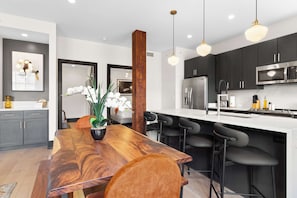 A modern kitchen with dark cabinets, a stainless steel refrigerator, a microwave, and a wooden dining table with bar stools.