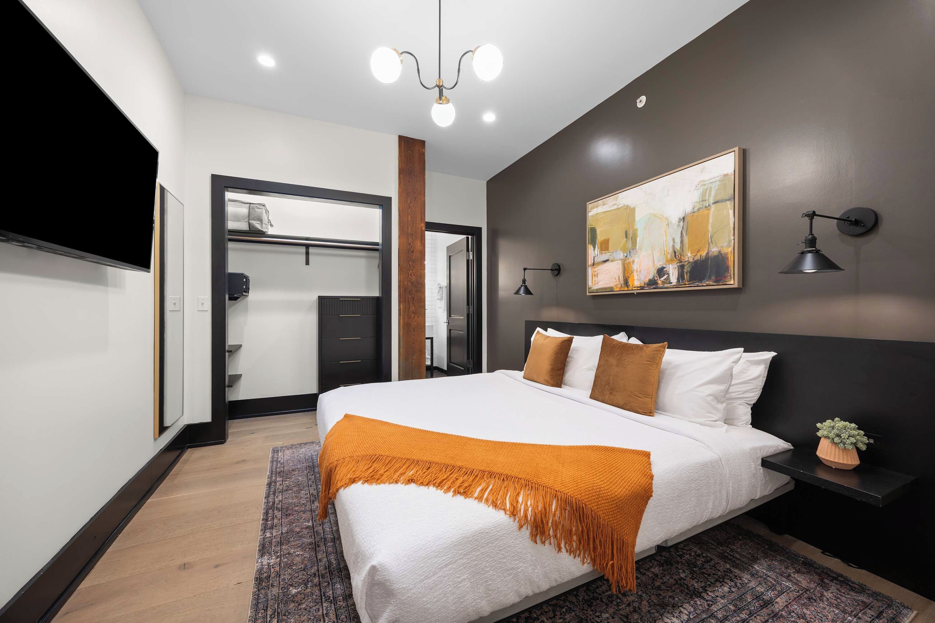 A modern bedroom with a large bed, a bedside table with a lamp, a painting on the wall, and a wardrobe.