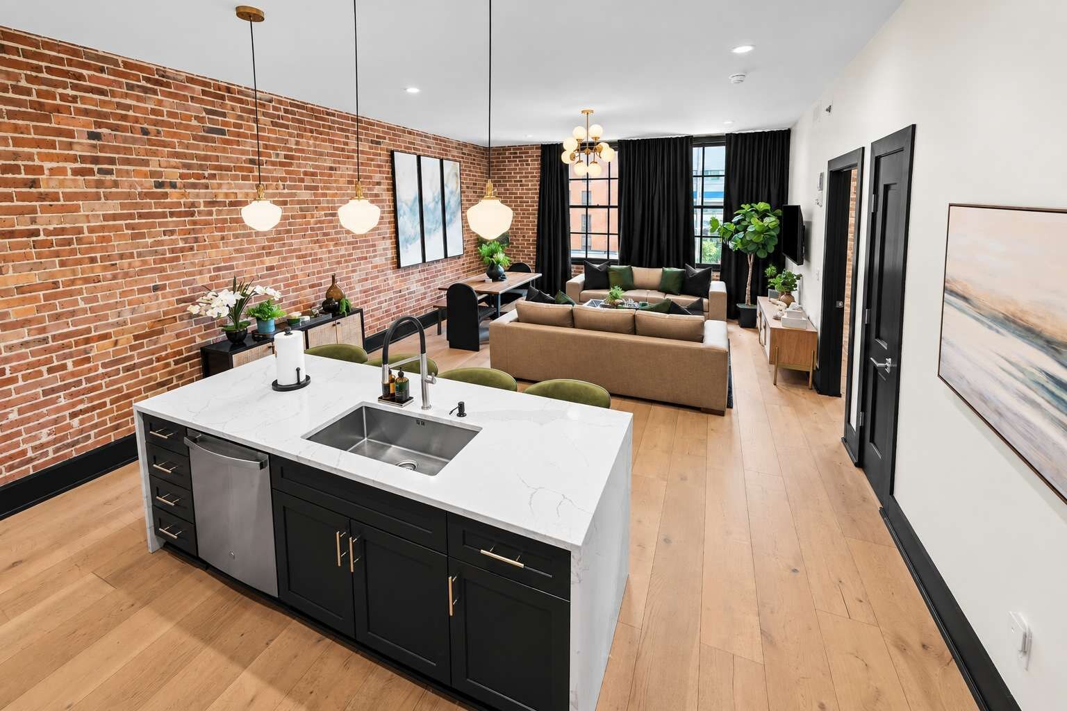 Une cuisine moderne avec un îlot central, des meubles de couleur noire et un mur en briques.
