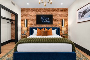 A hotel room with a brick wall, a bed with blue headboard, and a neon sign saying 'Enjoy today'. - Downtown Hotel 2 King Bed Suite | Gym | Rooftop (New Orleans)