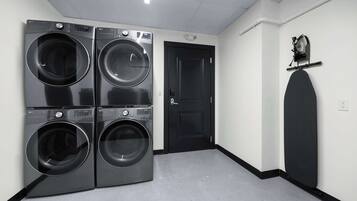 A laundry room with four stacked front-loading washing machines, a black door, and a wall-mounted drying rack.