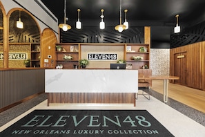 Ein Empfangsschalter mit einem Schild mit der Aufschrift 'ELEVEN48' und einem darunterliegenden Schild mit dem Text 'NEW ORLEANS LUXURY COLLECTION'.