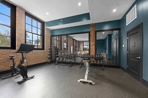 Ein Fitnessstudio mit Trainingsgeräten, großen Fenstern und einer Ziegelwand.