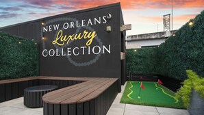 A wall with 'NEW ORLEANS Luxury Collection' signage, a wooden bench, and a miniature golf setup. - Bachelorette Suite Perfect for a Memorable Stay (New Orleans)