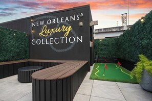 Eine Wand mit der Beschilderung 'NEW ORLEANS Luxury Collection', eine hölzerne Bank und eine Minigolf-Anlage.