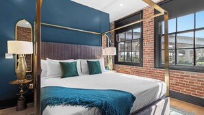 A modern hotel room with a large bed, two bedside tables with lamps, a view of the outside through a large window, and a brick wall. - All New | King bed | Gym | Rooftop (New Orleans)