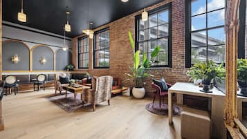 A spacious room with a brick wall, large windows, and a mix of seating including a sofa and chairs.