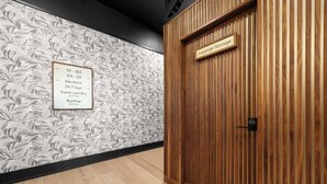 A hotel corridor with a wooden door labeled 'Luggage Storage' and a wall sign indicating amenities like elevators, a 24/7 gym, guest laundry, and a rooftop. - All New | King bed | Gym | Rooftop (New Orleans)