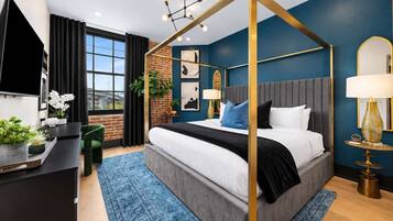 A modern bedroom with a four-poster bed, a desk with a computer, and a large window.