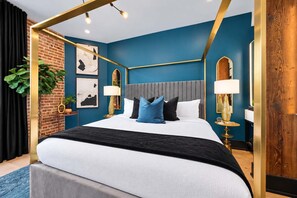 A modern bedroom with a four-poster bed, a brick accent wall, and a blue color scheme. - New Hotel | King bed | Gym | Rooftop (New Orleans)