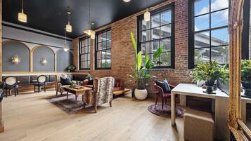 A spacious room with a brick wall, large windows, and a mix of seating including a sofa and chairs.