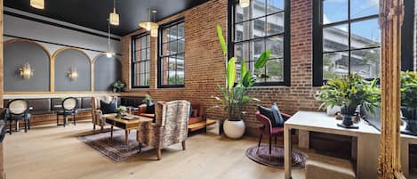 Amplia habitación con pared de ladrillo, ventanas grandes y una variedad de asientos, incluyendo un sofá y sillones.