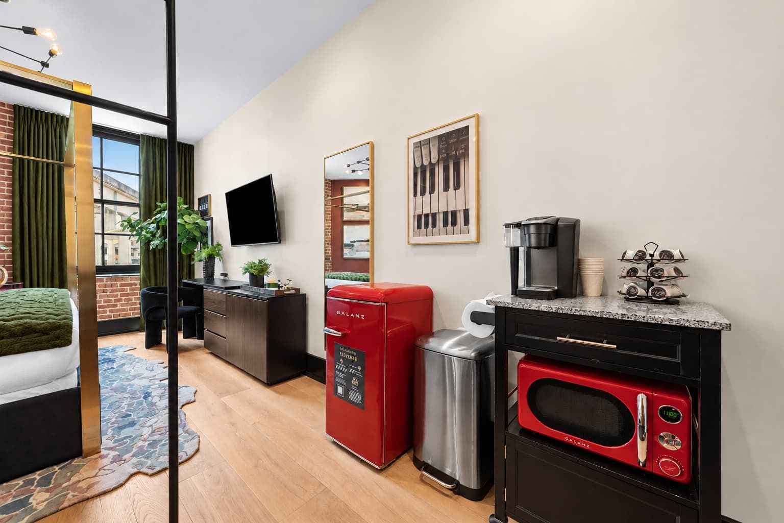 Une chambre d’hôtel de taille réduite, équipée d’un lit, d’un bureau, d’une machine à café, d’un four à micro-ondes et d’une poubelle.